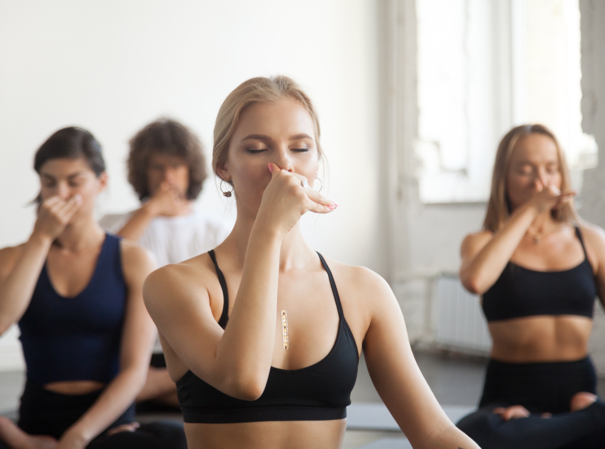 Group of young sporty people practicing yoga lesson with instructor, making Alternate Nostril Breathing, nadi shodhana pranayama exercise, sitting in Sukhasana pose, working out, indoor close up image